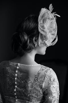Back of a woman with a fascinator in an embroidered dress.